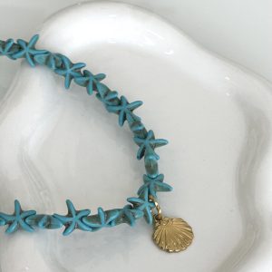 Κολιέ με τιρκουάζ αστερίες και χρυσό μενταγιόν κοχύλι πάνω σε λευκή επιφάνεια – boho καλοκαιρινό κόσμημα